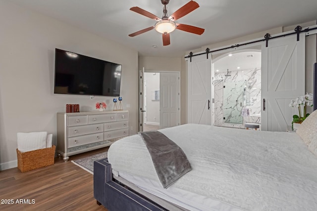 bedroom featuring ceiling fan, ensuite bathroom, a barn door, and dark hardwood / wood-style flooring