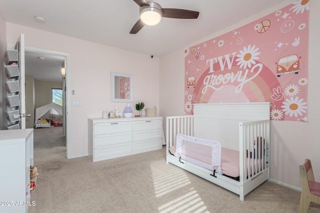 bedroom with ceiling fan, a nursery area, and light carpet