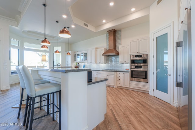 kitchen featuring white cabinets, decorative light fixtures, a raised ceiling, and wall chimney exhaust hood