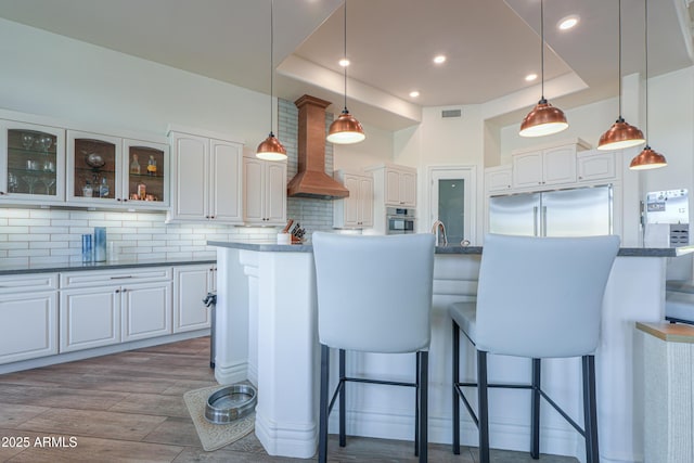 kitchen with a breakfast bar area, white cabinetry, wall chimney range hood, and appliances with stainless steel finishes