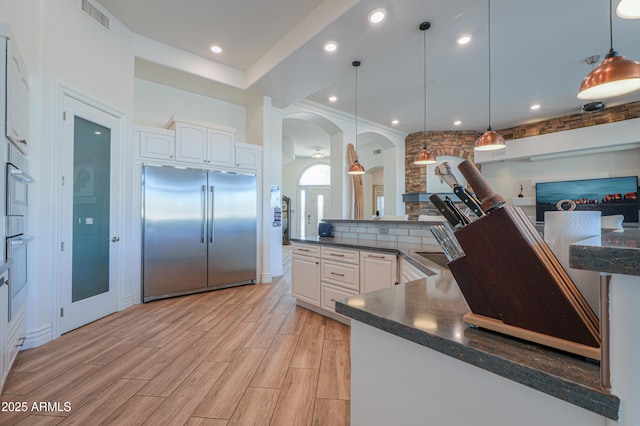 kitchen featuring kitchen peninsula, stainless steel appliances, pendant lighting, and white cabinetry