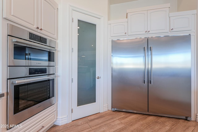 kitchen with appliances with stainless steel finishes, light hardwood / wood-style floors, and white cabinets