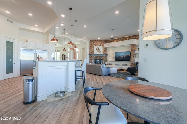 kitchen featuring hanging light fixtures, a breakfast bar area, white cabinets, built in refrigerator, and a fireplace