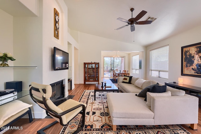 living room featuring light hardwood / wood-style flooring, ceiling fan with notable chandelier, and vaulted ceiling