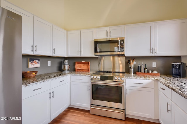 kitchen featuring light stone countertops, white cabinetry, stainless steel appliances, and light wood-type flooring