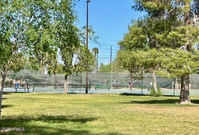 surrounding community featuring fence, a tennis court, and a lawn