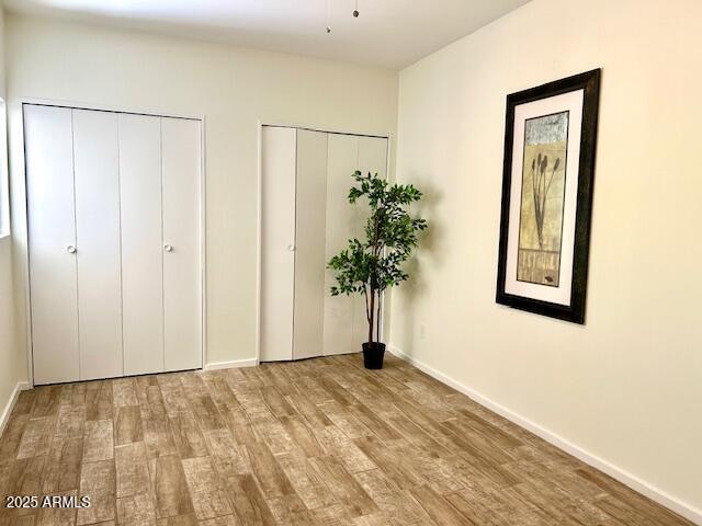 unfurnished bedroom featuring baseboards, multiple closets, and wood finished floors