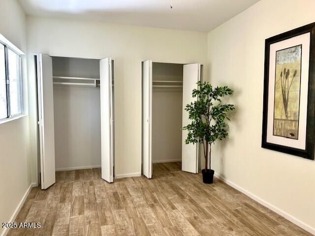 unfurnished bedroom with two closets, baseboards, and wood finished floors