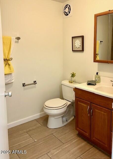 half bath with toilet, baseboards, visible vents, vanity, and wood finished floors