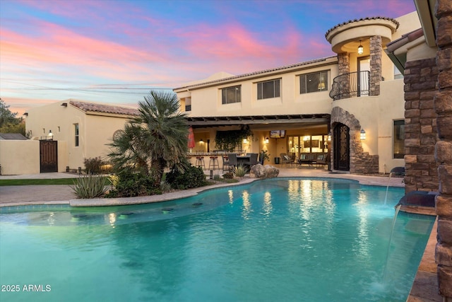 pool at dusk featuring pool water feature and an outdoor bar