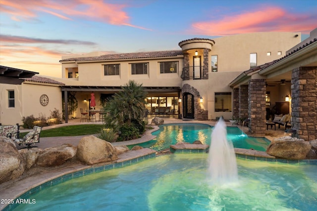 pool at dusk with pool water feature and ceiling fan