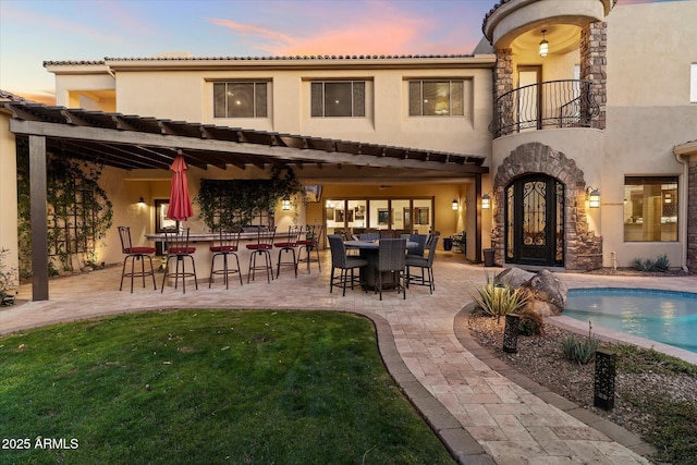 back house at dusk featuring a bar, a patio, and a balcony