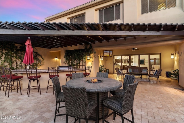 patio terrace at dusk with a bar, an outdoor hangout area, and ceiling fan