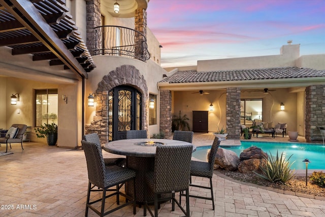 patio terrace at dusk featuring ceiling fan and a balcony