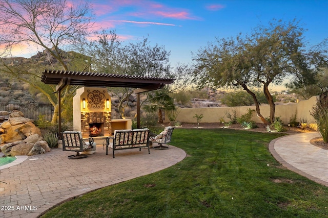 yard at dusk featuring an outdoor living space with a fireplace and a patio area