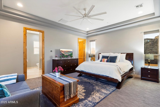 bedroom with a tray ceiling, connected bathroom, ceiling fan, and light carpet