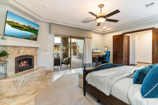 bedroom featuring ceiling fan, access to exterior, a fireplace, and a tray ceiling