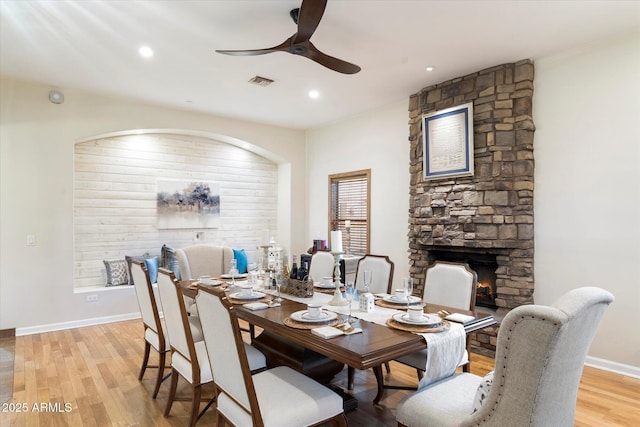 dining room with a fireplace, light wood-type flooring, and ceiling fan