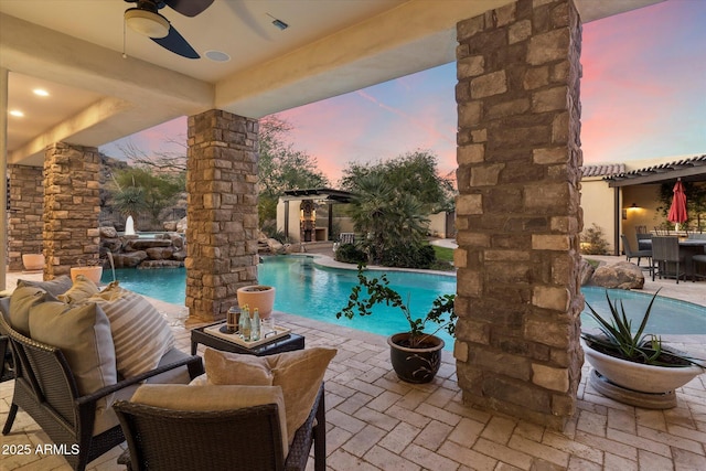 pool at dusk with pool water feature, ceiling fan, and a patio area