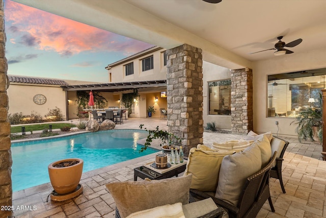 pool at dusk with ceiling fan and a patio area