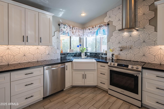 kitchen with dark countertops, decorative backsplash, appliances with stainless steel finishes, wall chimney exhaust hood, and a sink