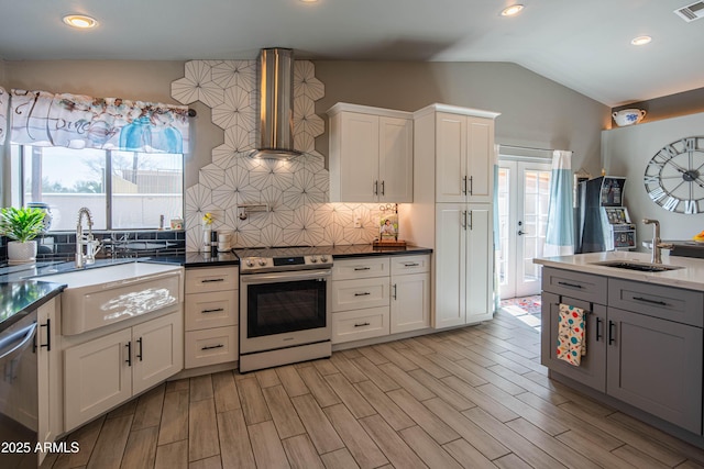 kitchen featuring vaulted ceiling, appliances with stainless steel finishes, wall chimney exhaust hood, and a sink