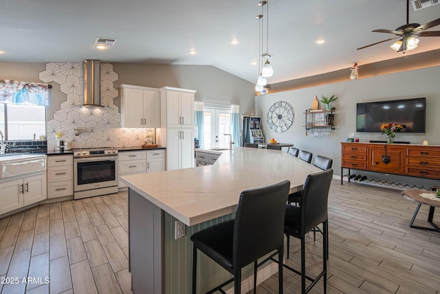 kitchen featuring visible vents, wood finish floors, electric range, vaulted ceiling, and wall chimney range hood