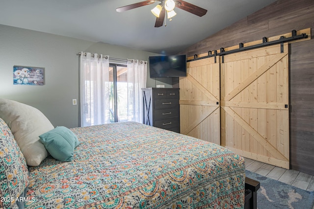 bedroom featuring a ceiling fan, a barn door, wood finished floors, and vaulted ceiling