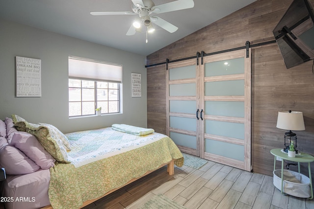 bedroom with wood finish floors, a barn door, wood walls, and vaulted ceiling