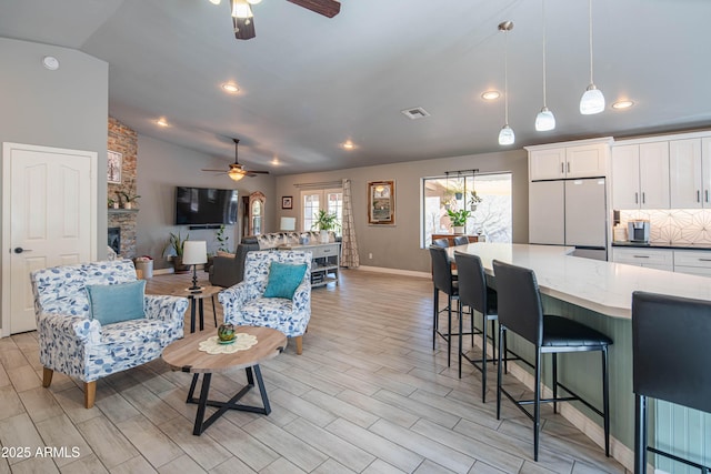 living room featuring a ceiling fan, visible vents, wood tiled floor, a stone fireplace, and vaulted ceiling