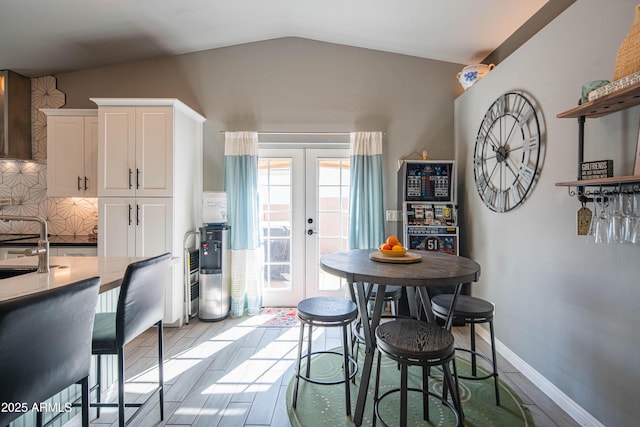 dining space featuring french doors, lofted ceiling, light wood-style floors, and baseboards