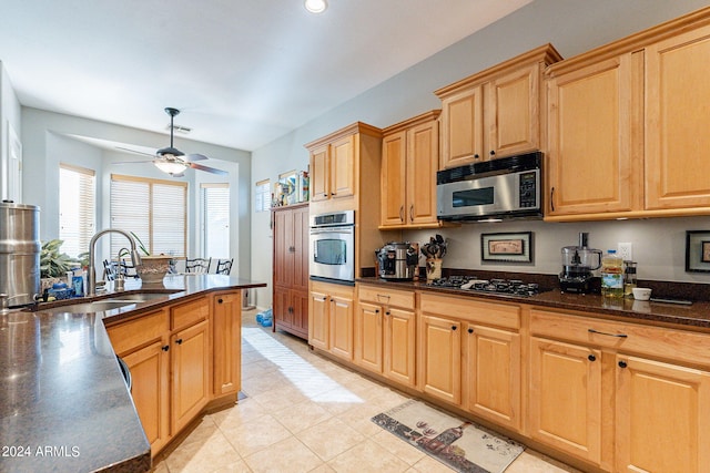 kitchen with appliances with stainless steel finishes, light tile patterned floors, ceiling fan, dark stone counters, and sink