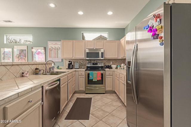 kitchen with appliances with stainless steel finishes, backsplash, sink, light tile patterned floors, and tile countertops