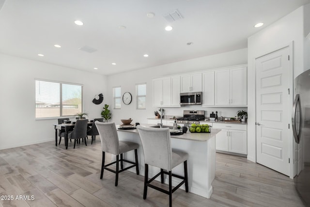 3089 N 200th Ave, Buckeye, AZ 85396 - kitchen featuring stainless steel appliances, a breakfast bar, light wood-type flooring, a center island with sink, and white cabinetry