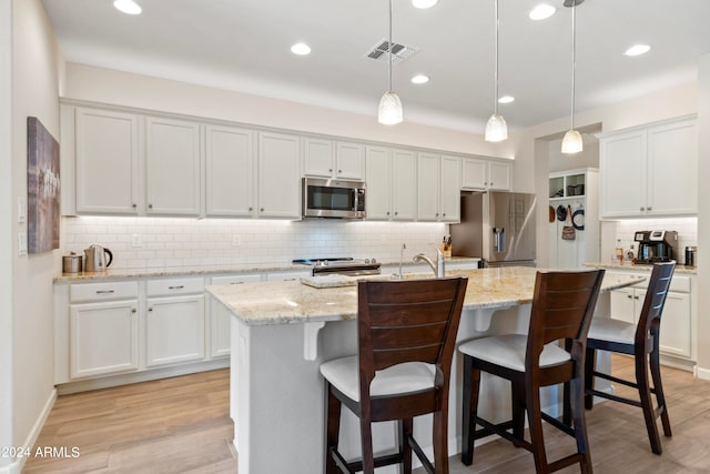 kitchen featuring an island with sink, hanging light fixtures, white cabinetry, stainless steel appliances, and light wood-type flooring