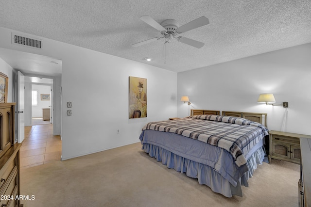 bedroom with ceiling fan, light colored carpet, and a textured ceiling