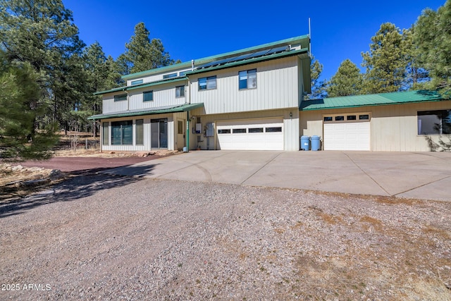 view of front of home with solar panels, a garage, driveway, and metal roof