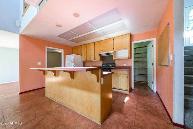 kitchen featuring baseboards, a breakfast bar, freestanding refrigerator, under cabinet range hood, and range