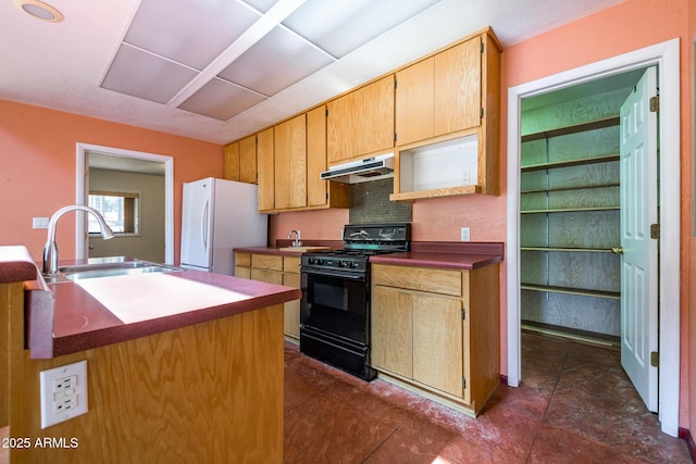 kitchen with gas stove, freestanding refrigerator, a sink, under cabinet range hood, and dark countertops