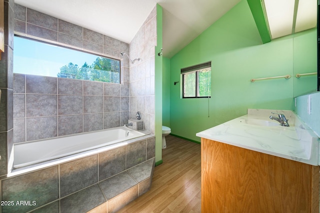 bathroom with vanity, wood finished floors, lofted ceiling, tiled shower / bath combo, and toilet