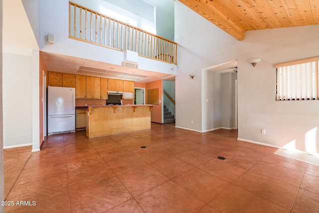 unfurnished living room with stairway, baseboards, wood ceiling, and a towering ceiling