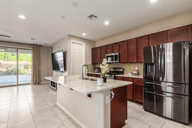 kitchen featuring tasteful backsplash, an island with sink, light stone countertops, sink, and stainless steel appliances