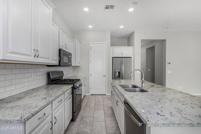 kitchen with appliances with stainless steel finishes, white cabinetry, sink, backsplash, and a center island with sink