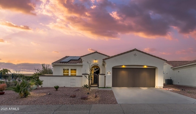 mediterranean / spanish home featuring a garage, roof mounted solar panels, driveway, and stucco siding