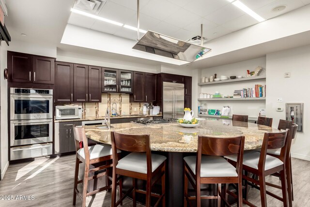 17139 S 174th Dr, Goodyear, AZ 85338 - kitchen with a paneled ceiling, light wood-style floors, dark brown cabinetry, a warming drawer, and appliances with stainless steel finishes