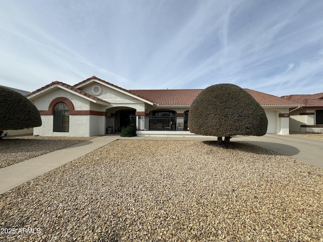 mediterranean / spanish-style home with stucco siding, driveway, a tile roof, a gate, and a fenced front yard