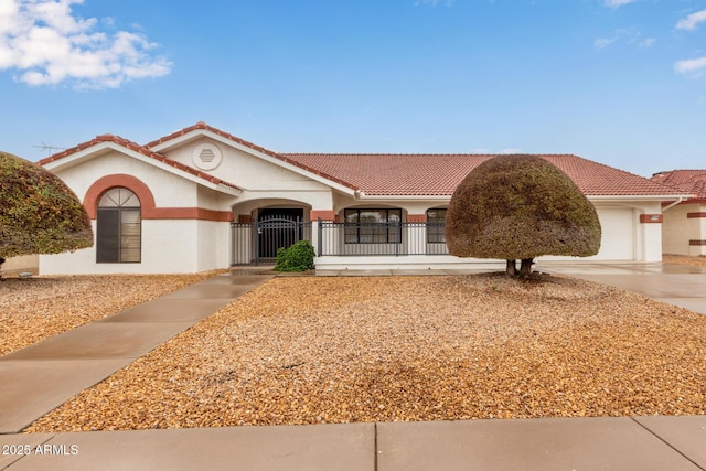 mediterranean / spanish house featuring stucco siding, a tile roof, a gate, a fenced front yard, and an attached garage