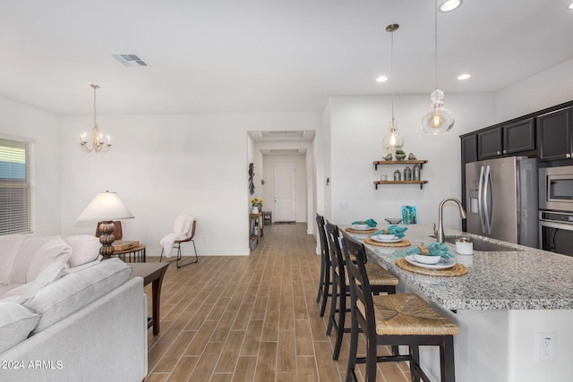 kitchen featuring sink, a breakfast bar area, decorative light fixtures, stainless steel appliances, and light stone countertops