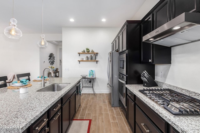 kitchen with appliances with stainless steel finishes, decorative light fixtures, sink, light stone counters, and wall chimney range hood