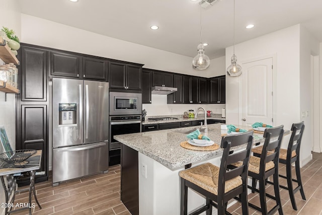 kitchen featuring sink, a breakfast bar area, hanging light fixtures, stainless steel appliances, and light stone countertops